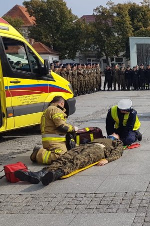 Policjant oraz ratownik medyczny udzielają pomocy osobie leżącej, poszkodowanej w zdarzeniu drogowym.