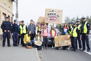 Policjanci stojący wraz z uczniami biorącymi udział w działaniach promujących bezpieczne zachowania na drodze