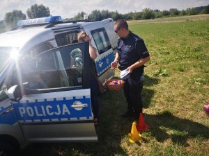 policjant trzyma w ręku koszyk z cukierkami i ulotki i rozmawia z uczestniczką festynu