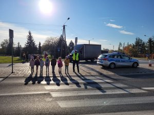 policjant i dzieci przechodzą przez jezdnię na przejściu dla pieszych