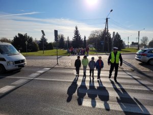 policjant i dzieci przechodzą przez jezdnie na przejściu dla pieszych