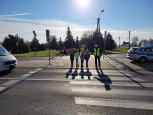 policjant z dziećmi przechodzą przez jezdnię na przejściu dla pieszych