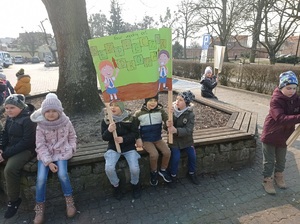 dzieci siedzą na ławce z banerem