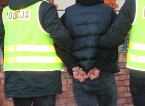 policjanci prowadzą mężczyznę z kajdankami założonymi na ręce z tyłu