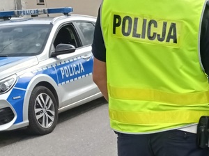 policjant stoi przy oznakowanym radiowozie