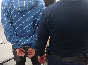 policjant pilnuje zatrzymanego, który ma założone kajdanki na ręce trzymane z tyłu