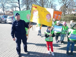 dzieci i policjant pozują do zdjęcia z kolorowymi plakatami
