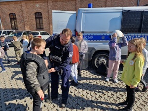 policjant pomaga założyć chłopcu czarną kamizelkę służbową