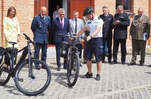 policjant, którego obserwują osoby stojące obok trzyma rower