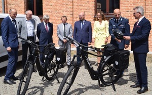 osoby stoją przy białym samochodzie i dwóch rowerach