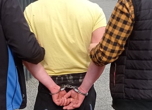 policjanci prowadzą zatrzymanego z założonymi kajdankami na ręce z tyłu