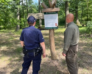 policjant i leśniczy obserwują teren leśny