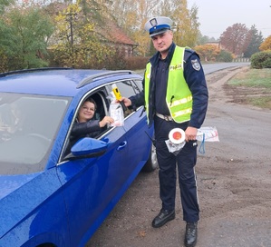 policjant ruchu drogowego pozuje do zdjęcia przy kobiecie, której wręcza upominek