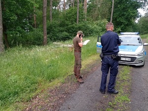 policjant i leśniczy stoją w lesie przy radiowozie